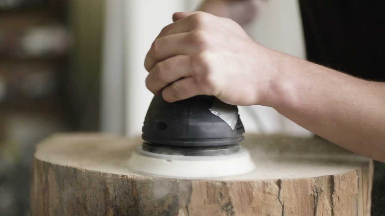 Primer plano de manos lijando un tronco de madera con una lijadora orbital