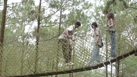 young asian friends crossing rope bridge in forest adventure