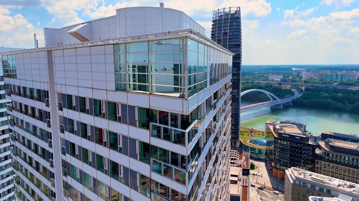 Bratislava, Slovacchia, 2 giugno 2026: Primo piano della facciata in vetro di un moderno grattacielo, Bratislava. Vista dettagliata con drone di finestre e balconi su un grattacielo contemporaneo con un ponte fluviale sullo sfondo.
