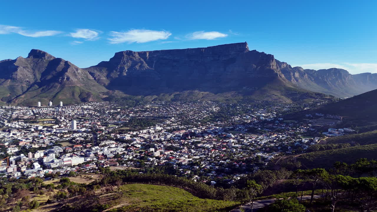 Cinematic aerial view of Table Mountain and Cape Town cityscape, showcasing rugged cliffs, urban sprawl, and South Africa’s iconic natural landmark under clear blue sky