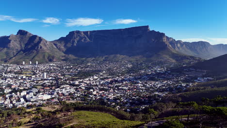cinematic aerial view of table mountain and cape town cityscape, showcasing rugged cliffs, urban sprawl, and south africa’s iconic natural landmark under clear blue sky