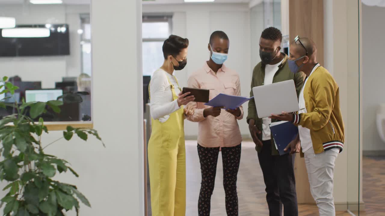 Diverse group of male and female business colleagues wearing face masks, working in office