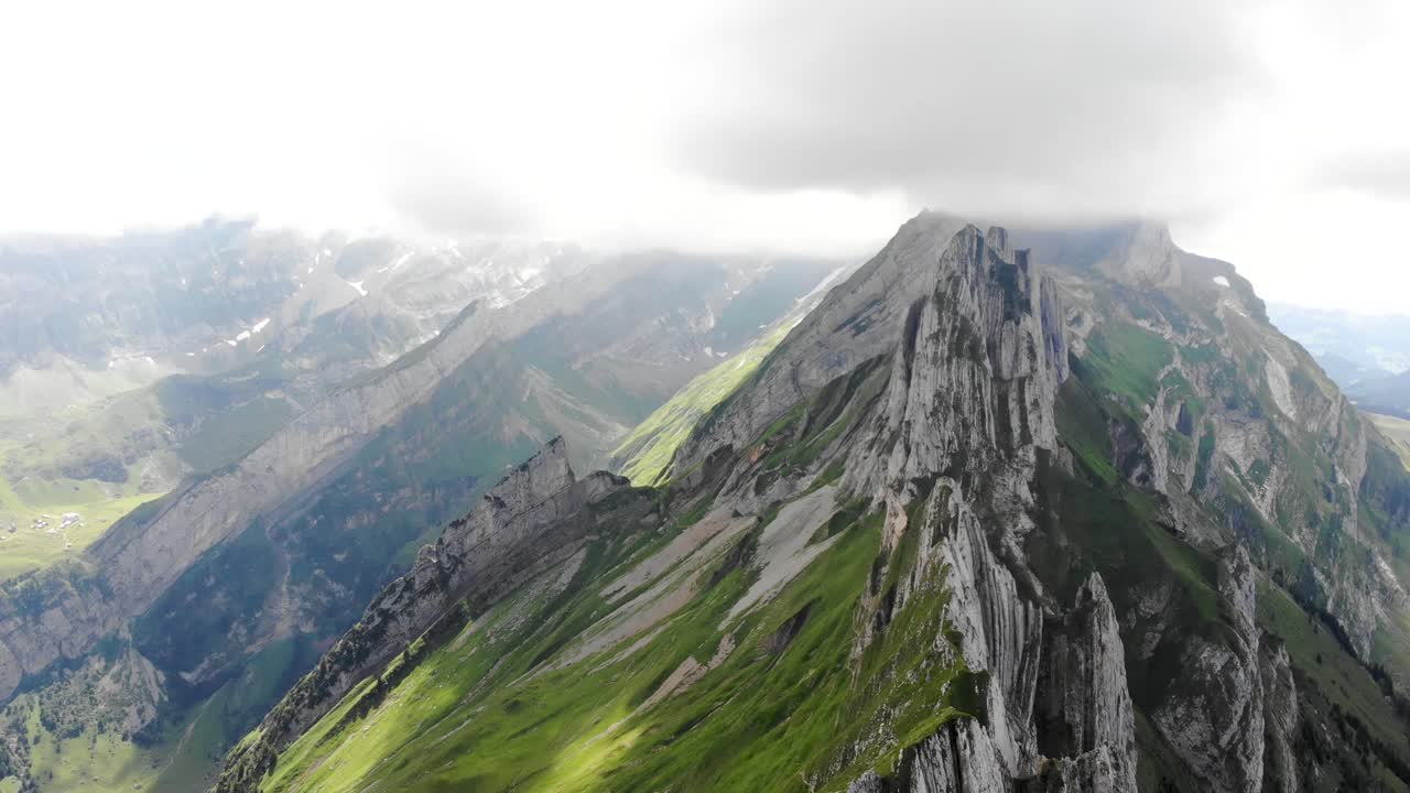 sobrevuelo aéreo sobre y lejos de los acantilados de schafler ridge en appenzell, suiza con acantilados, picos montañosos y exuberantes laderas verdes de verano a la vista