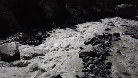 Drone-aerial-view-of-a-river-in-the-Swiss-alps-with-strong-current-making-the-water-muddy-and-rocks-on-the-riverbed