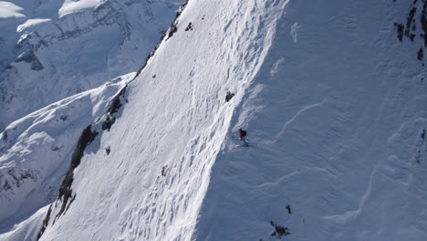 Aerial-orbit-shot-of-professional-skier-waiting-on-snowy-steep-slope-of-mountain-during-sunny-day