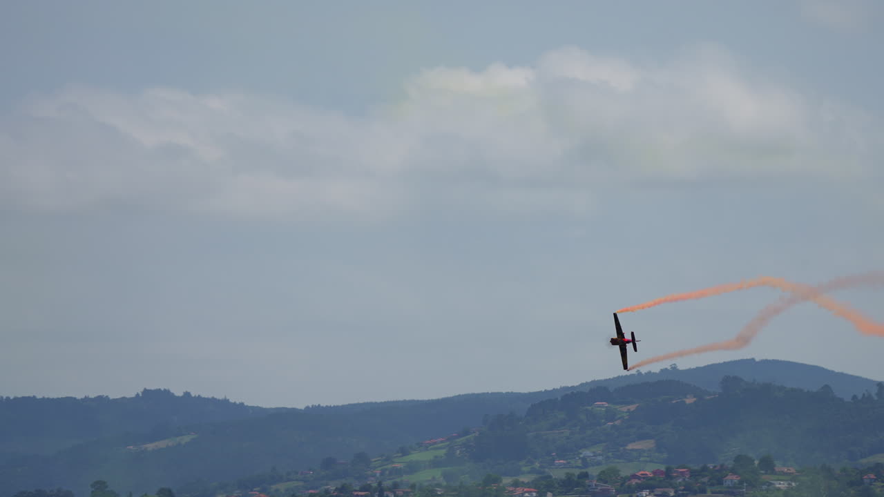 Single airplane with orange smoke trail performing aerial stunt above green hills during airshow