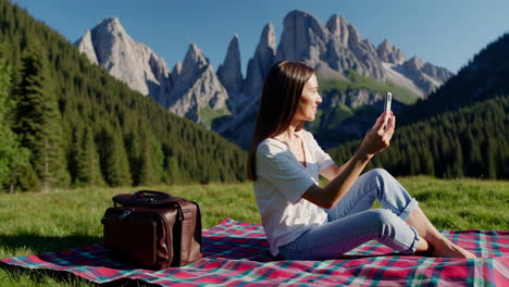 woman using cell phone on picnic blanket in mountains