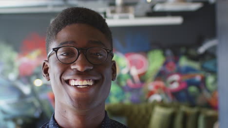 young black man smiling to camera in front of mural in creative workplace, close up, head shot