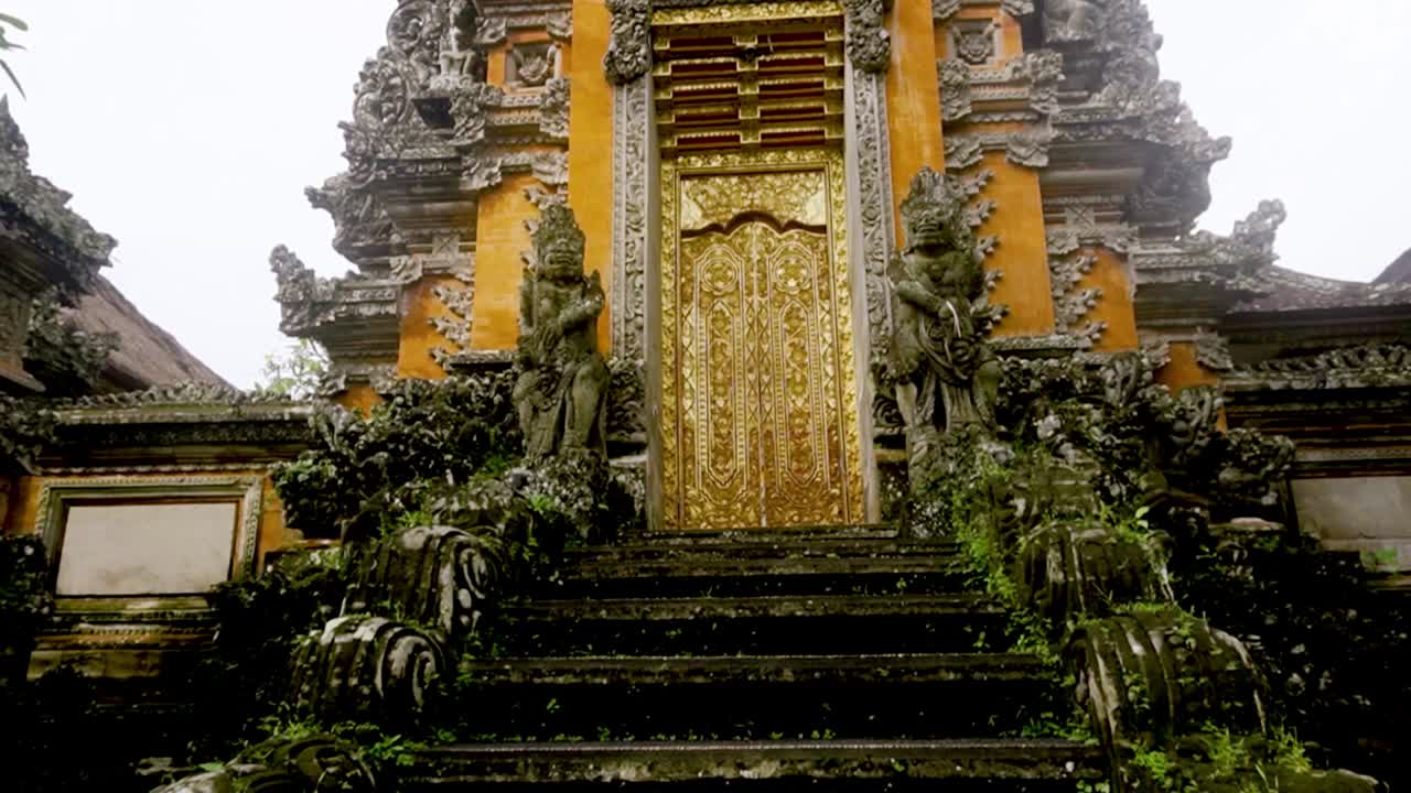 ジャングルと曇り空の中にそびえる、豪華な金のサラスワティ寺院の階段がチルトアップで現れる。