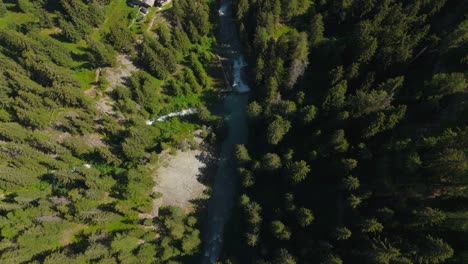 a waterfall flowing through dense forest in the italian alps, aerial view