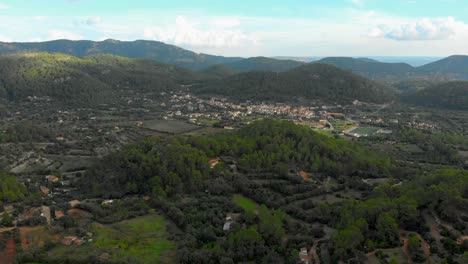 Drohnenaufnahmen-über-Einem-Tal,-Das-Sich-In-Richtung-Einer-Kleinen-Stadt-Mit-Bergen-Im-Hintergrund-Bewegt