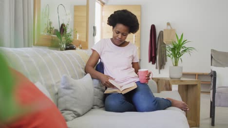 Feliz-Mujer-Afroamericana-Sentada-En-El-Sofá,-Leyendo-Un-Libro