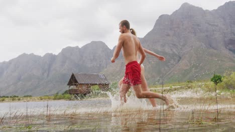 Caucasian-couple-having-a-good-time-on-a-trip-to-the-mountains,-wearing-bathing-suits,-running-and-j