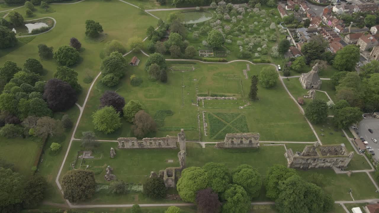 Aerial view of Glastonbury abbey ruins, drone moving forward and camera facing down over the abbey gardens,. 4K, 60fps.