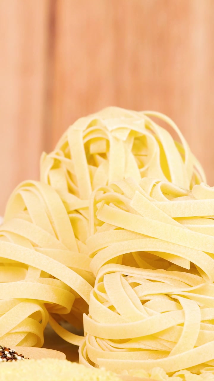 Una mano sistema nidi di tagliatelle su una superficie di legno sotto una luce calda, creando una scena culinaria rustica.