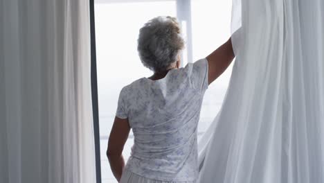 african american senior woman opening curtains of her window at home