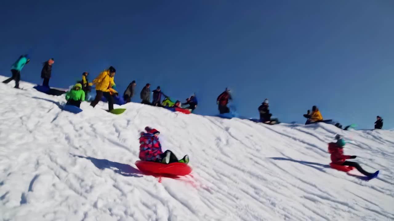 A lively video capturing people sledding down a snowy hill. Shot from a low angle, it highlights