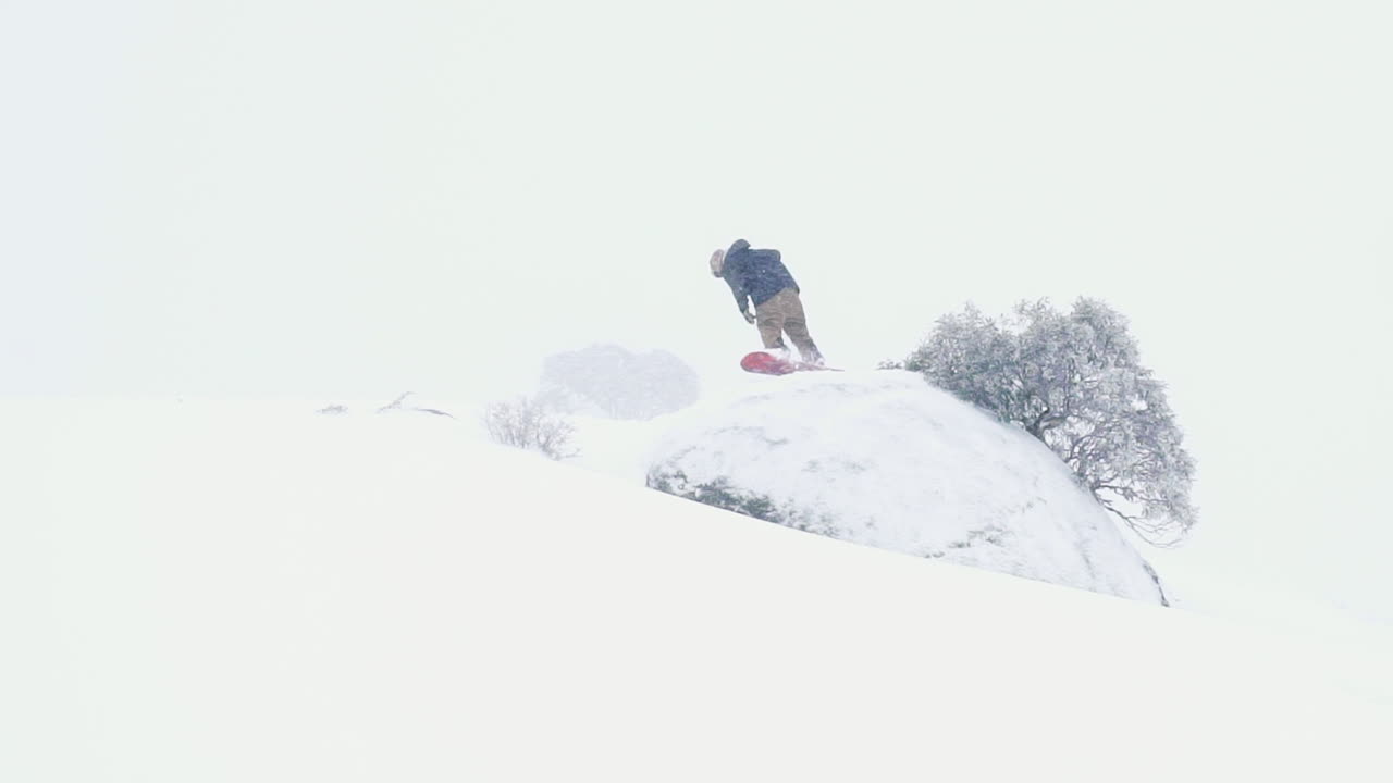 2017년 7월 perisher guthega 스키장에서 동료들과 눈보라가 몰아치는 겨울날 젊은 호주 스노보더가 공중 기동에서 스핀을 수행합니다.