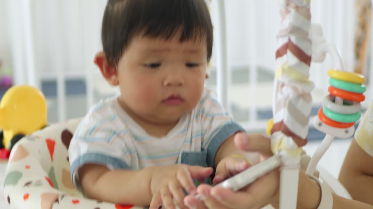 A baby girl explores her surroundings while interacting with a smartphone in a vibrant setting.