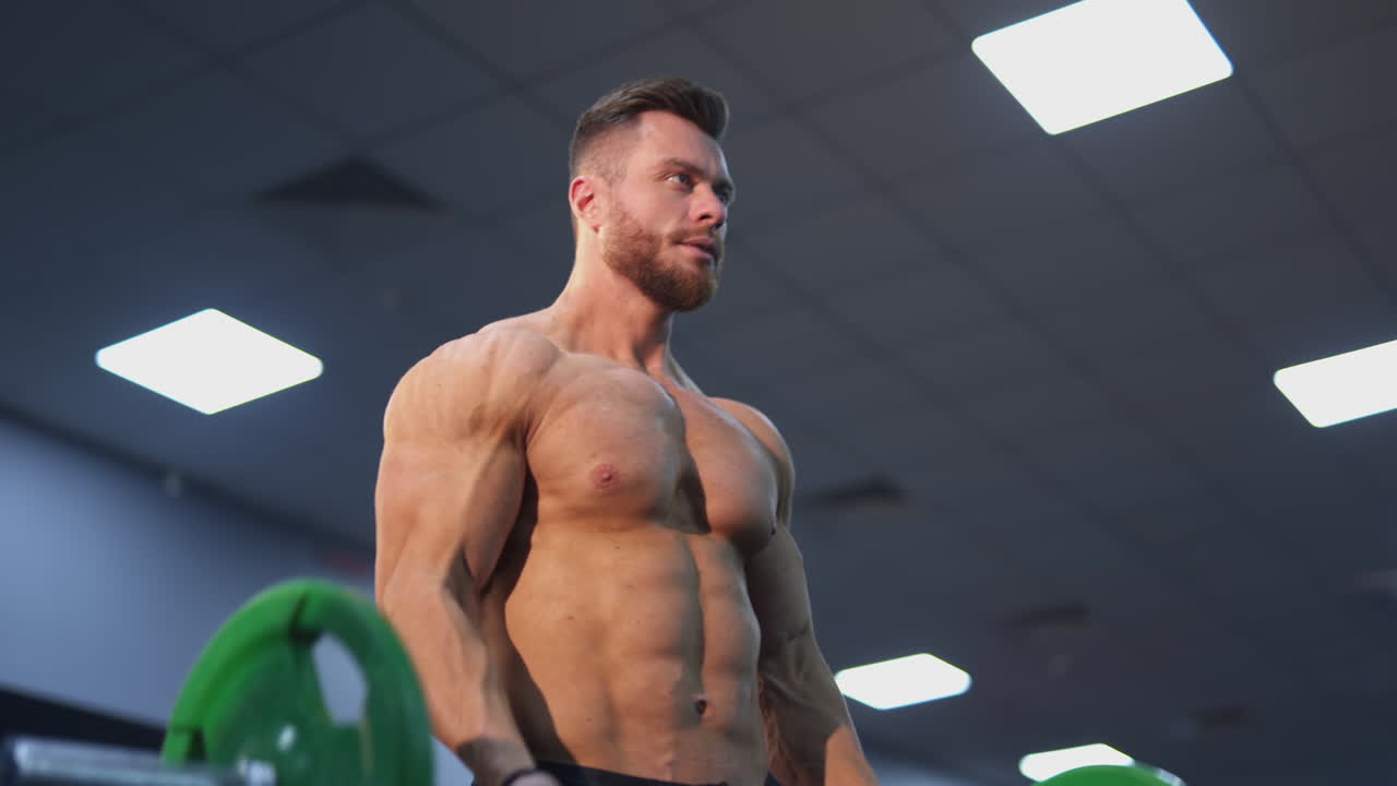Shirtless athlete pumping muscles with a barbell. Sportsman doing weightlifting exercise in fitness gym. Healthy lifestyle. Close-up.
