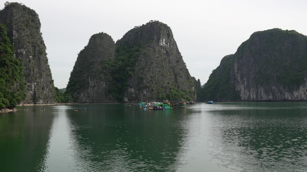 Cruise over calm water with floating village, view of tall karst limestone islands, Cat Ba, Vietnam