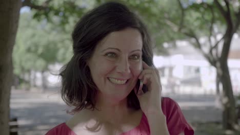 Smiling-middle-aged-woman-talking-on-smartphone-in-park