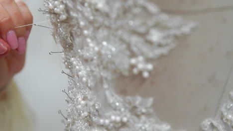 Close-up-fashion-designer-for-brides-in-his-Studio-pins-needles-lace-wedding-dress.-Seamstress-creates-an-exclusive-wedding-dress.-Secure-with-pins-and-needles-outline.-Small-private-business.-Sew-rhinestones-and-crystals-to-the-dress-thread-and-needle.-Jewelry-work.