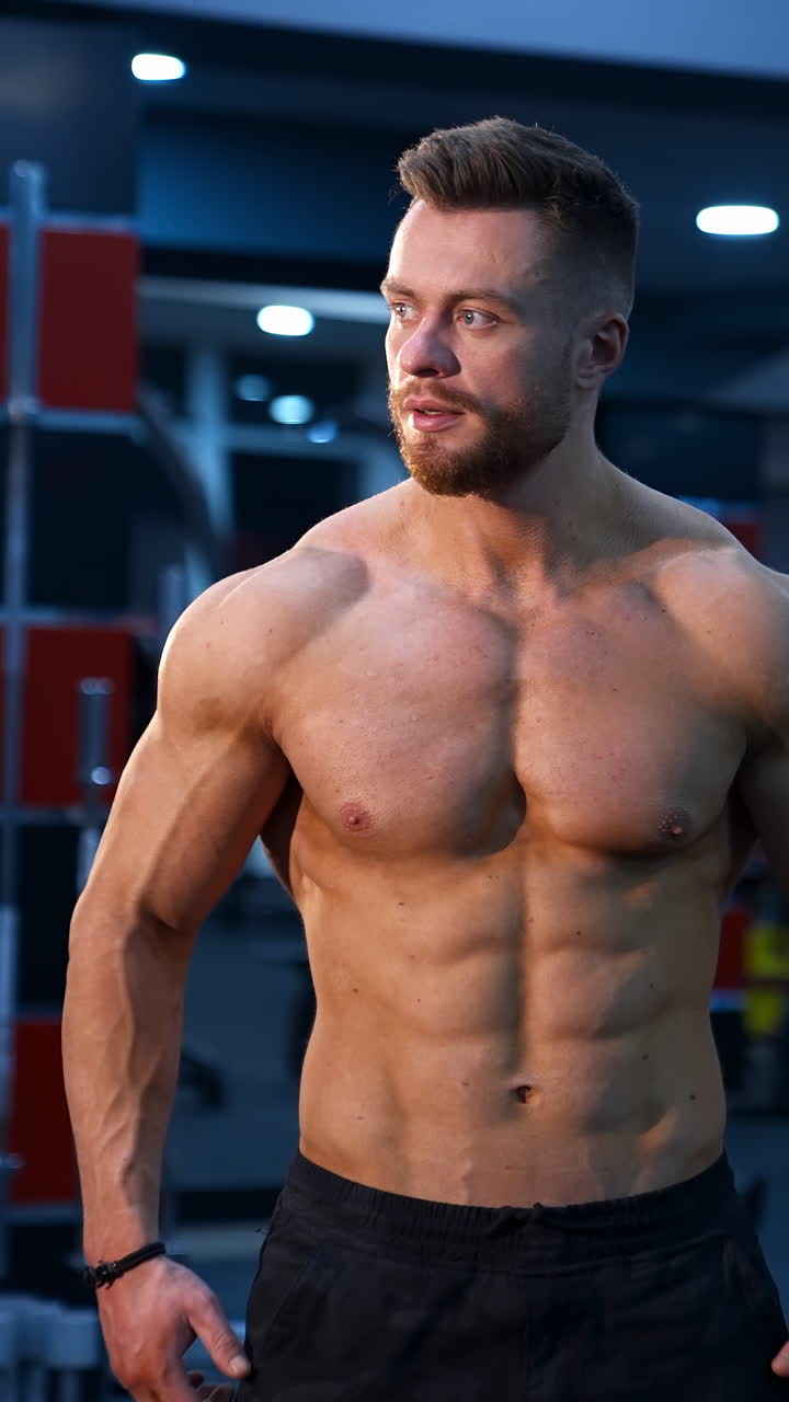 Muscle athlete strongman pumps muscules in a gym after heavy training. Perfect torso with strong abs. Handsome power male with naked torso. Vertical video