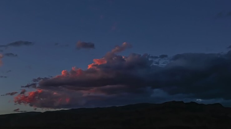 Sunset illuminates changing cloud formation over mountain ridge at blue hour