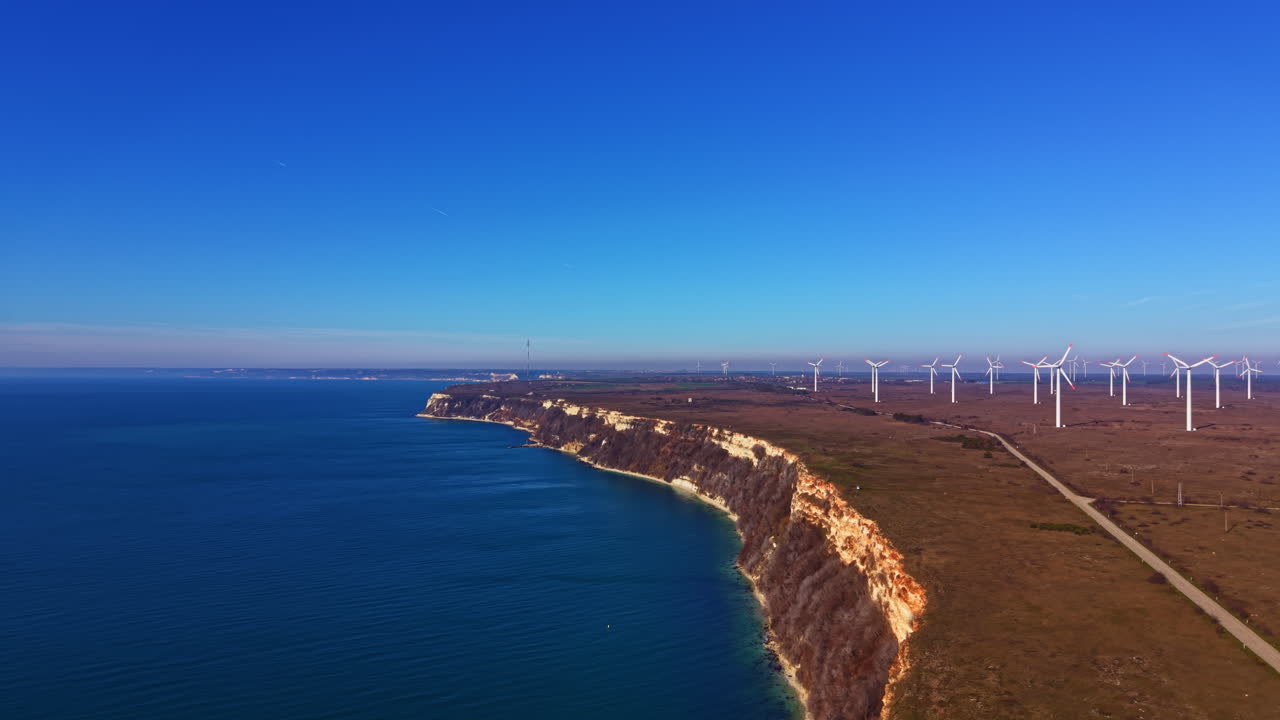 Vista sulla costa con turbine eoliche e cielo terso sull'oceano durante le ore diurne vicino a un'area naturale