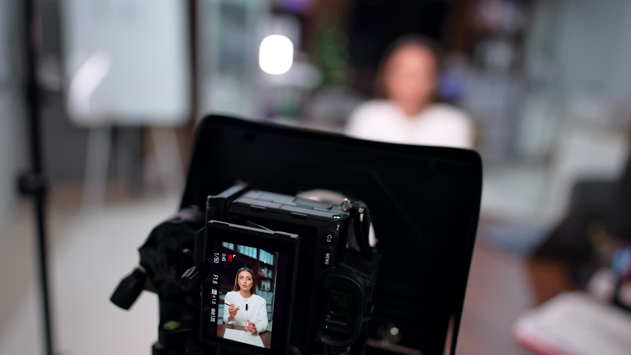Modern camera filming a brunette woman. Close up high-angle view on the equipment used at blog content creation. Blurred backdrop.