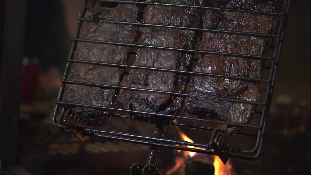 아르헨티나 파타고니아에서 바베큐에서 고기 조각을 는, 활기찬 불꽃이 아래에서 춤을 추는, 야외에서 진정적이고 맛있는 요리 경험을 만니다.