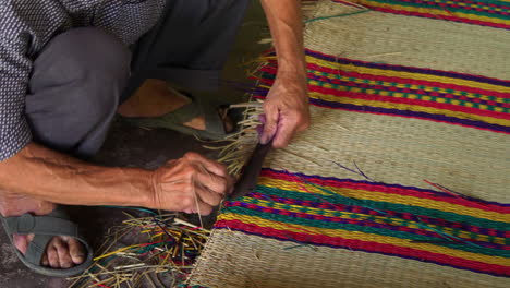 hombre asiático haciendo a mano un colchón tejido de tela colorida, de cerca