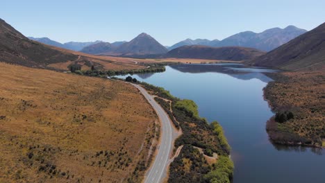 aerial drone view of a beautiful scenic valley with asphalt road next to the crystal clear blue lake surrounded by hills and mountains on a clear sunny day in 4k