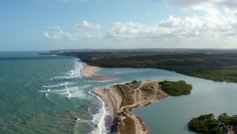 Descending-aerial-drone-wide-shot-of-the-beautiful-coastline-of-Gramame-where-the-ocean-meets-the-river-near-the-tropical-beach-capital-city-of-Joao-Pessoa-in-Paraiba,-Brazil-on-a-warm-summer-day