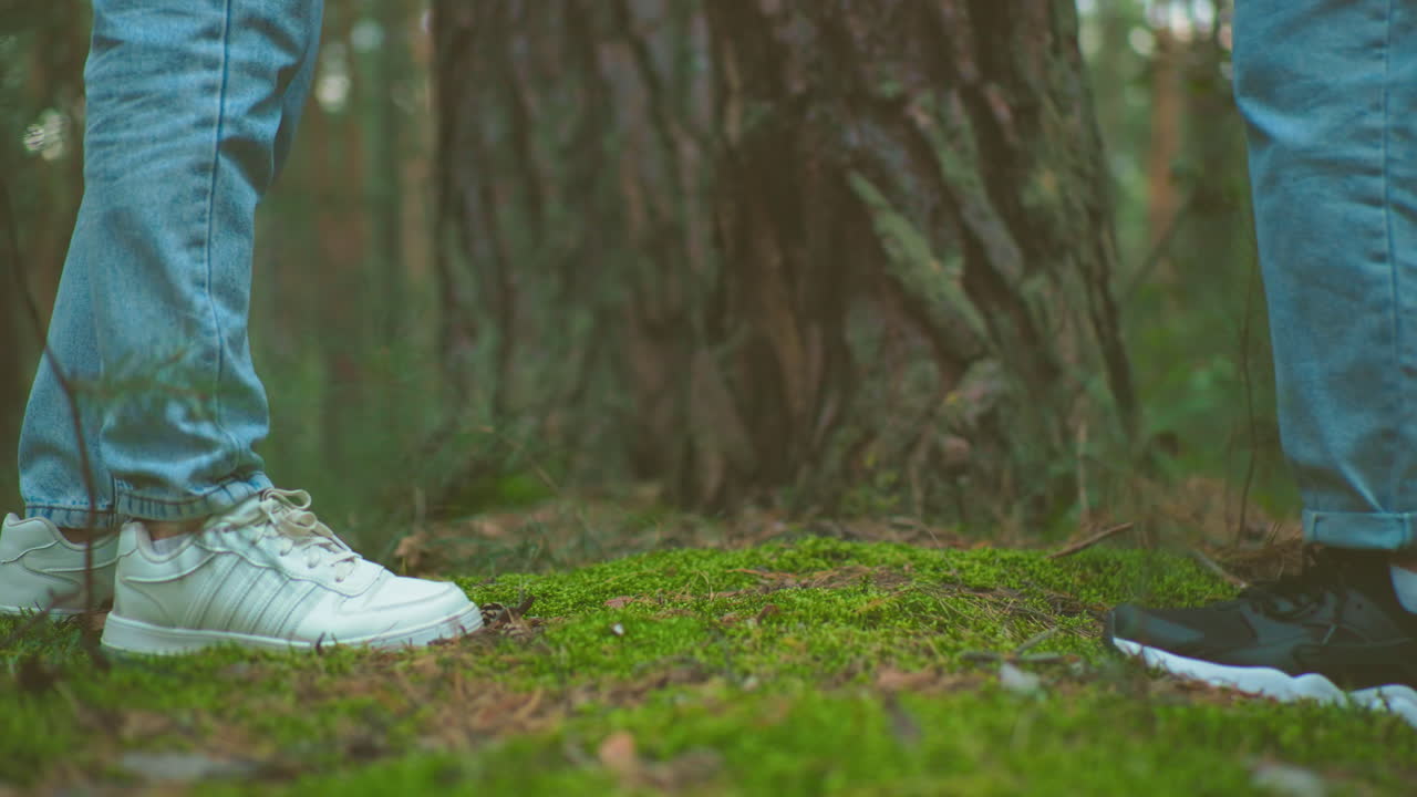 Close-up of women in jeans and sneakers zipping up backpacks retrieved from forest ground, preparing for hike, mossy terrain and tall trees create peaceful, natural setting