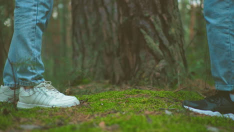 primer plano de mujeres con vaqueros y zapatillas deportivas cerrando las mochilas recuperadas del suelo del bosque, preparándose para la caminata, el terreno de musgo y los árboles altos crean un entorno pacífico y natural