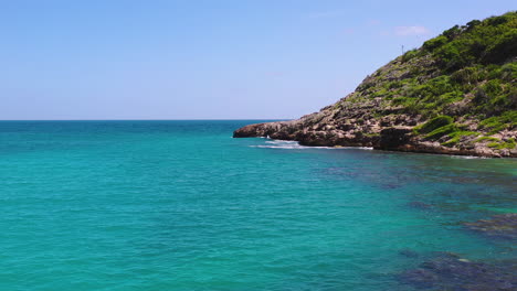 rocky cliffs of the half moon bay of the antigua island in the caribbean sea above the turquoise waters on a sunny summer day with a cloudless sky, moving aerial shot 4k