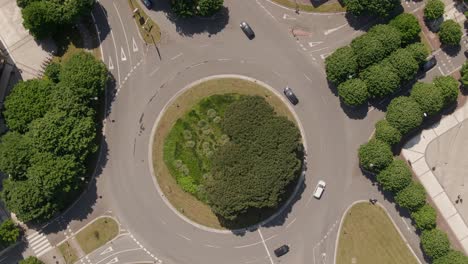 City-traffic-on-green-and-vibrant-roundabout,-top-down-rotate-view