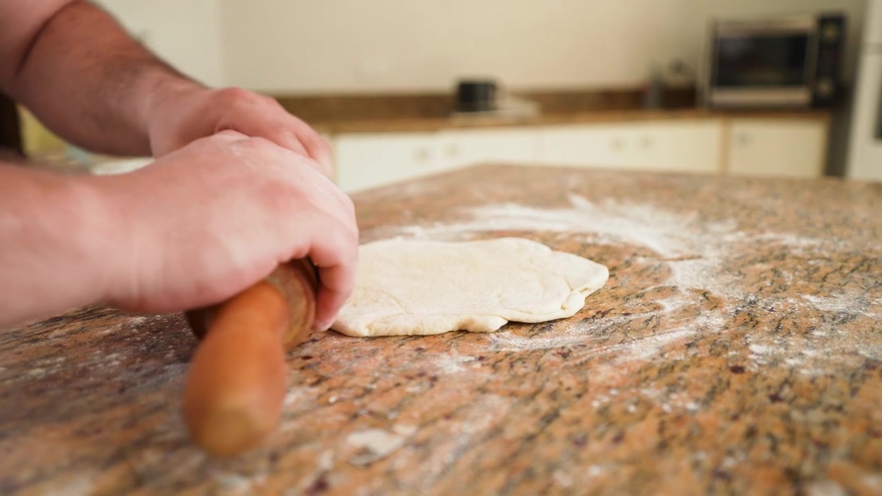 Uno chef prepara l'impasto per pizza su un piano di lavoro infarinato, impastandolo per ottenere la consistenza ideale per una crosta di pizza croccante e gommosa.