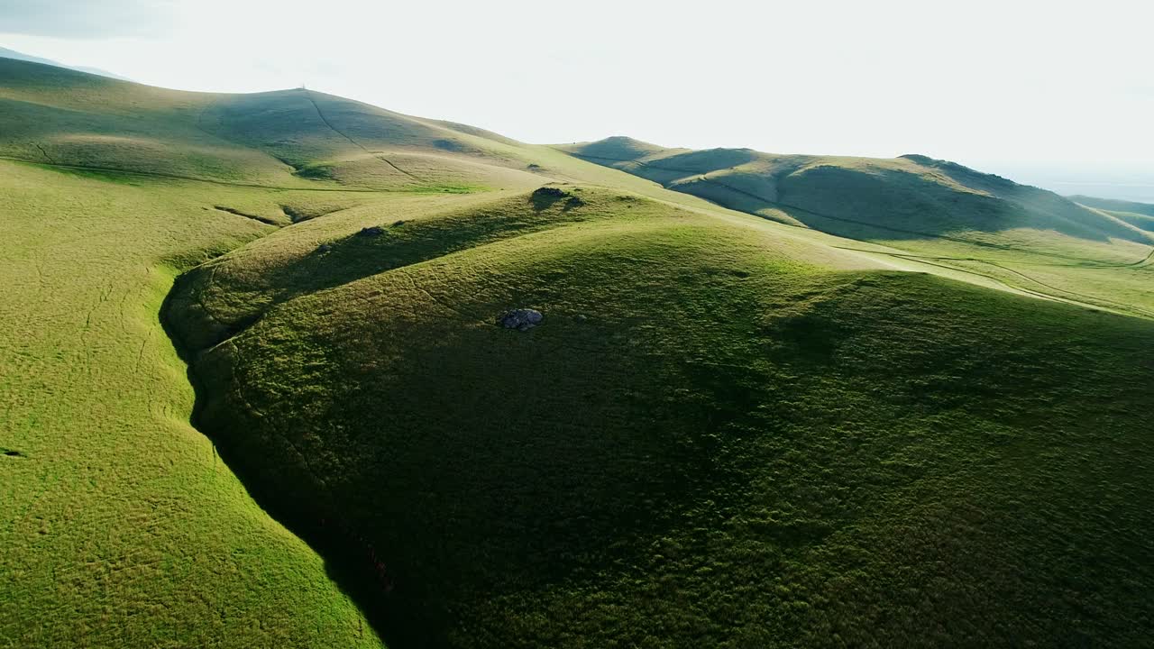 Drone footage of a vast landscape of lush, undulating hills under a clear sky