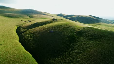 drone footage of a vast landscape of lush, undulating hills under a clear sky