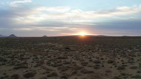 vehículo todoterreno bajando por un sendero de tierra en el desierto de mojave al atardecer - vista aérea