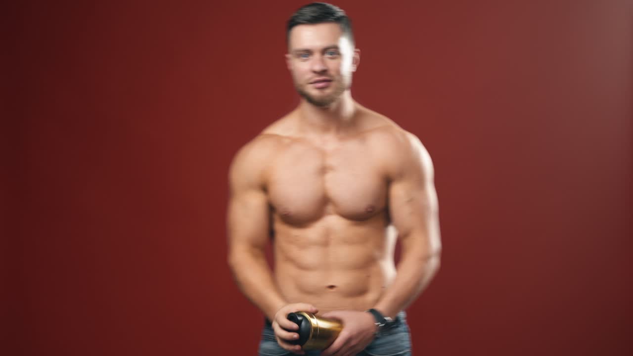 Attractive bodybuilder guy with protein shake. Portrait of a sportsman with muscular body. Shirtless sportsman showing golden flask and his arm biceps in studio.