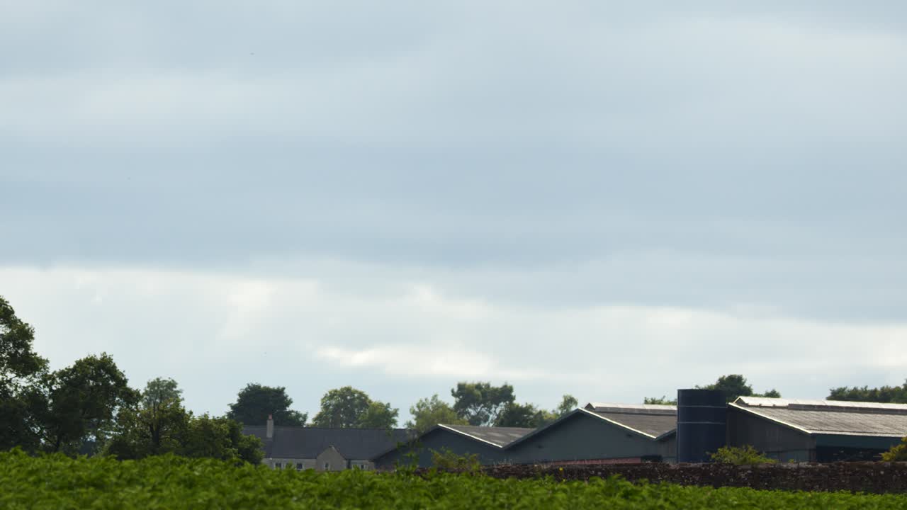Wind turbine blades spin steadily above rural landscape, cloudy daylight, smooth lateral camera pan