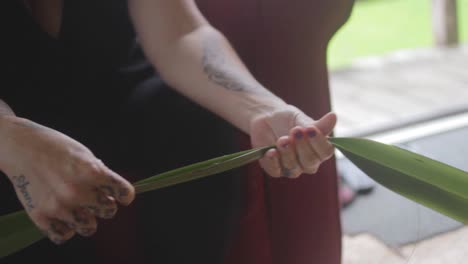 a woman is prepping plant leaves to weave a basket