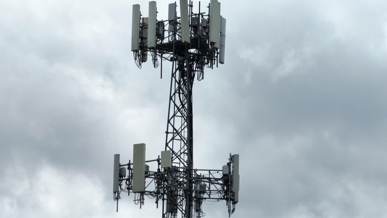 Proud American flag waves in wind before a cell tower rising into a cloudy sky. Powerful symbol of freedom, modern communication, and technological spirit of the United States