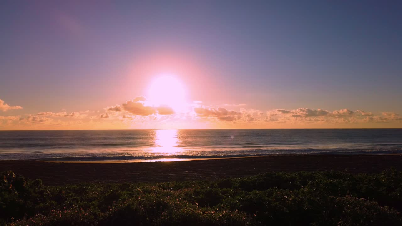 UHD Hawaii Kauai timelapse static of sunrise over the ocean with a few people on beach in distance on partly cloudy morning
