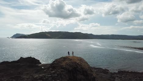 aerial 4k travellers standing on top of ocean peninsula point, indonesia