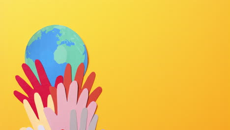 close up of hands together with globe made of colourful paper on yellow background with copy space